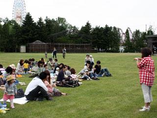 広場の芝生で各々レジャーシートを広げて話をしている人たちの写真