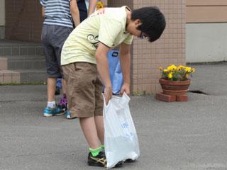 屋外で前かがみになり重そうに給水袋を持っている児童の写真
