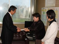 男性に寄付金を渡している女性とそれを見て微笑んでいる白いセーターを着た女性の写真