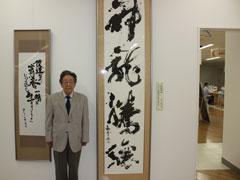 書道作品2点の間に立っているスーツ姿の新谷様の写真