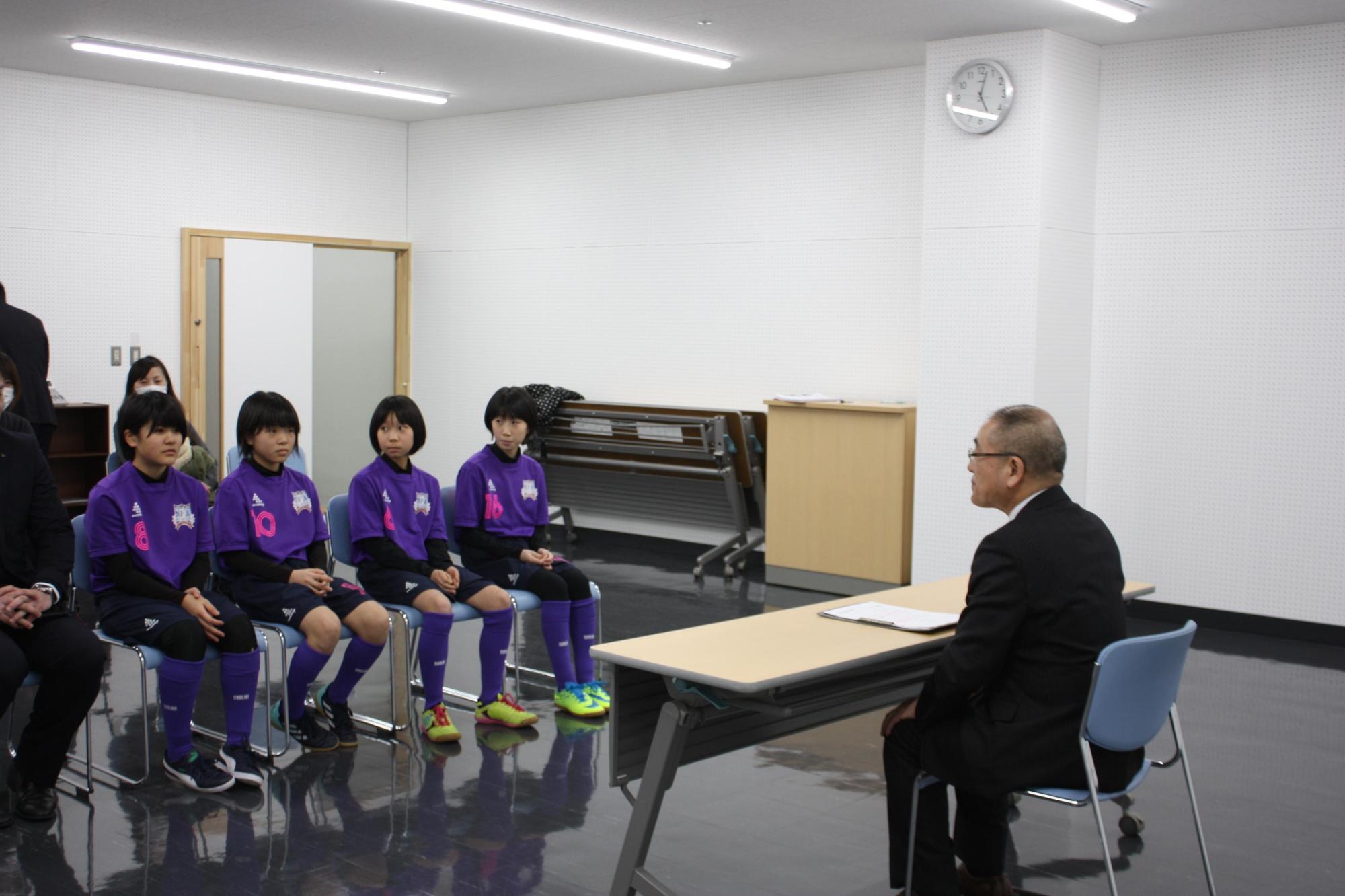 全国大会に出場する選手たちが、教育長と椅子に座って向かい合い、話をしている写真