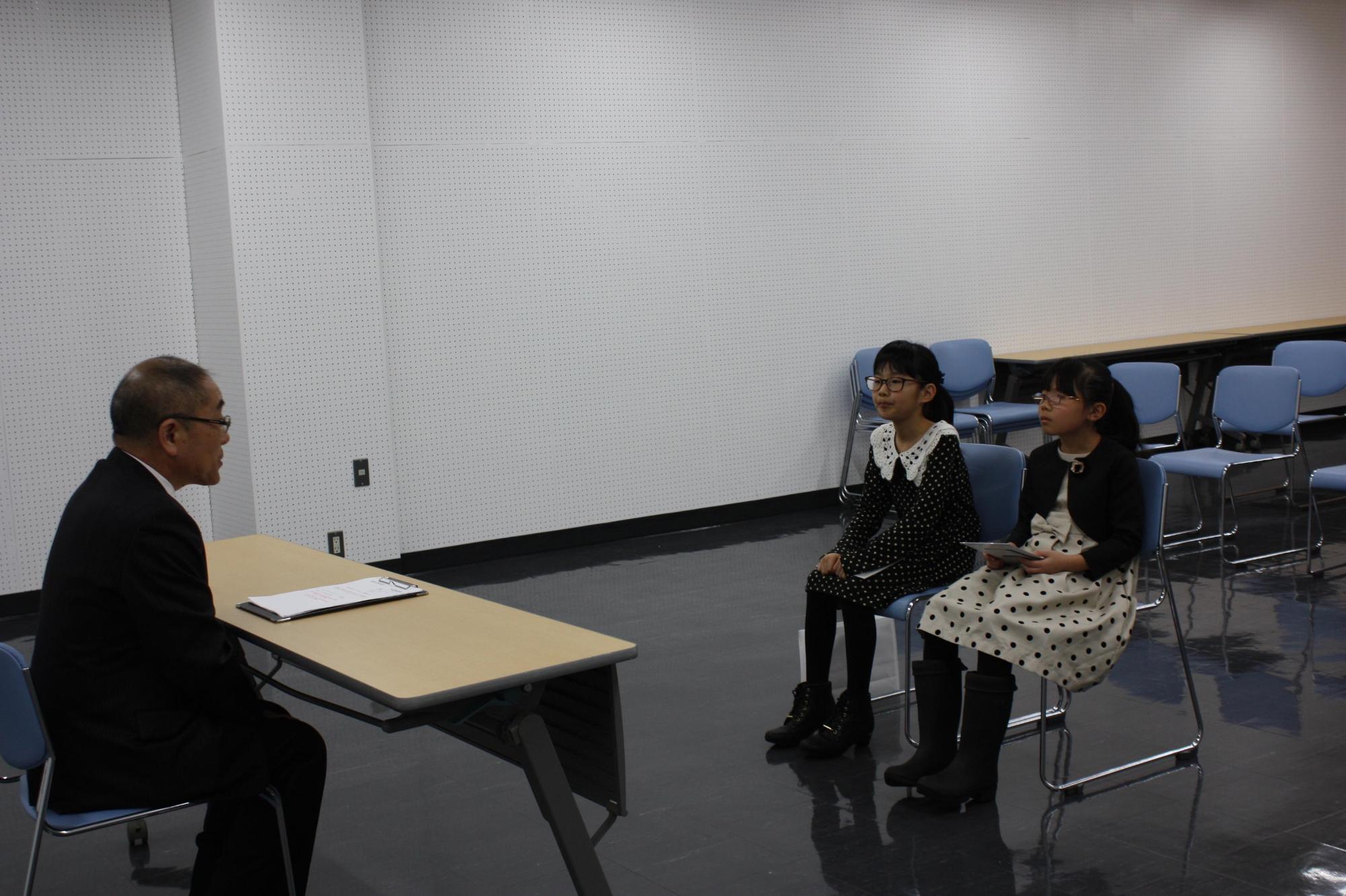 ピアノコンクールに出場した女の子2名が教育長と椅子に並んで向かい合っている写真