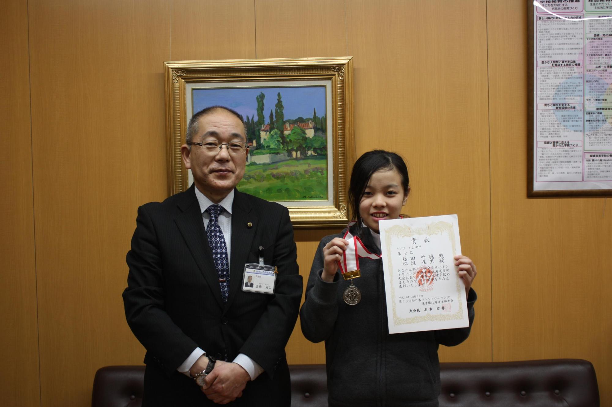 教育長室で、立ち上がり賞状とメダルを掲げているバトンワーリング藤田選手の写真