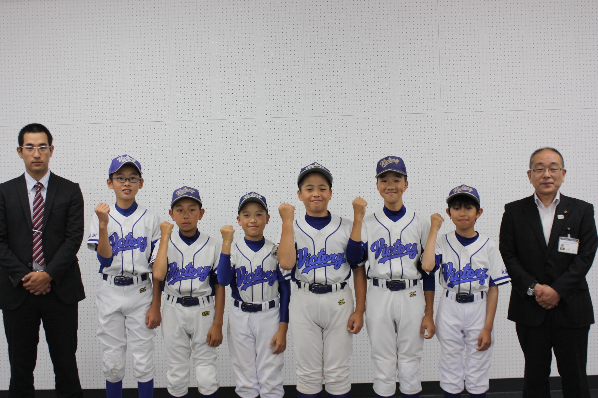 ユニフォーム姿で立つてポーズをとる岩見沢南ビクトリーの小学生野球チームのメンバーと教育長の写真