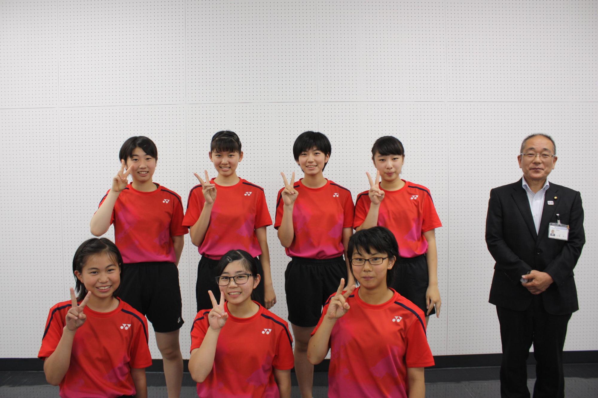 バドミントン全国大会に出場するユニフォーム姿の学生と教育長の集合写真