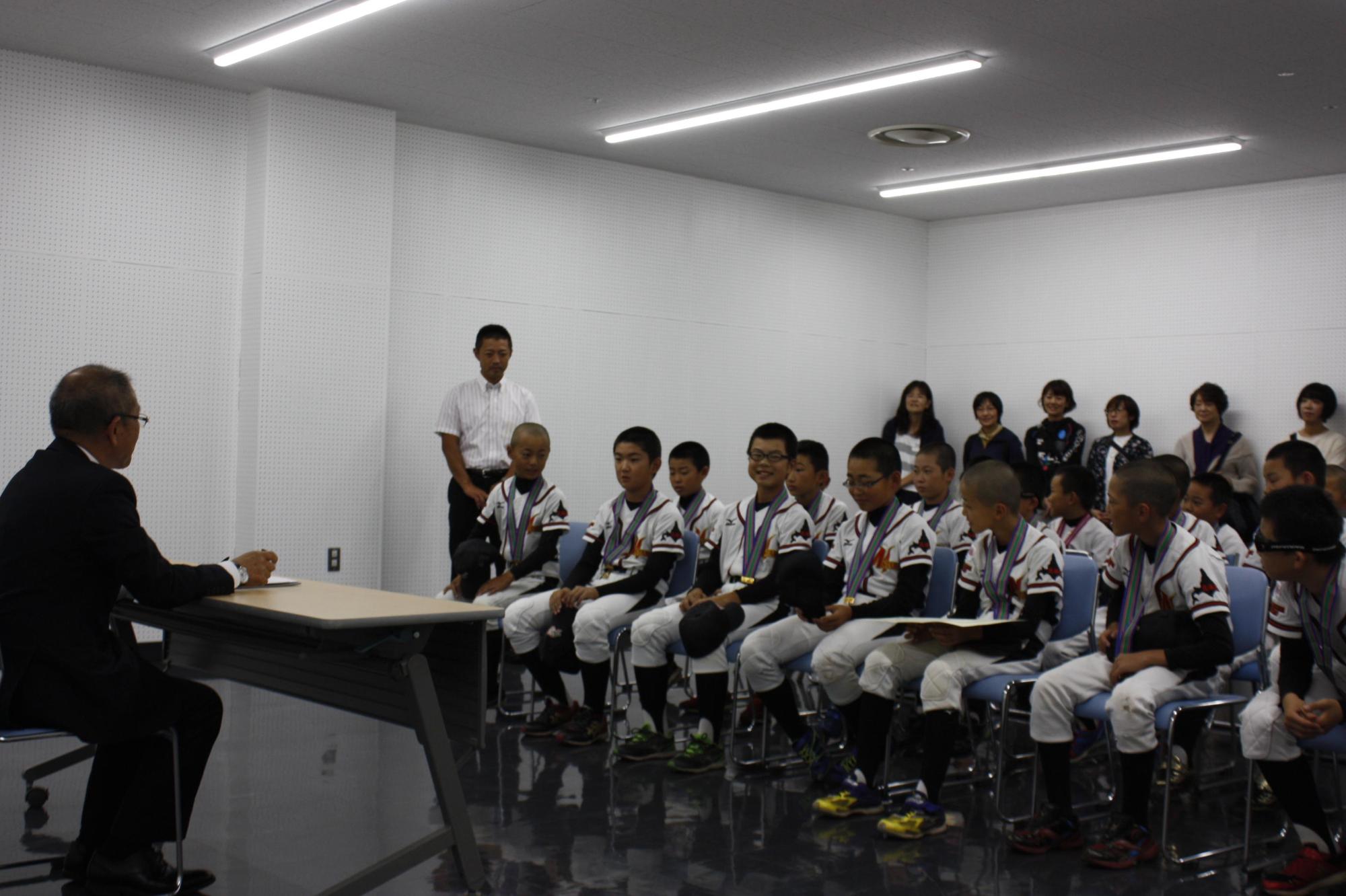 教育長に表敬訪問している軟式リトルリーグの野球団の選手たちの写真