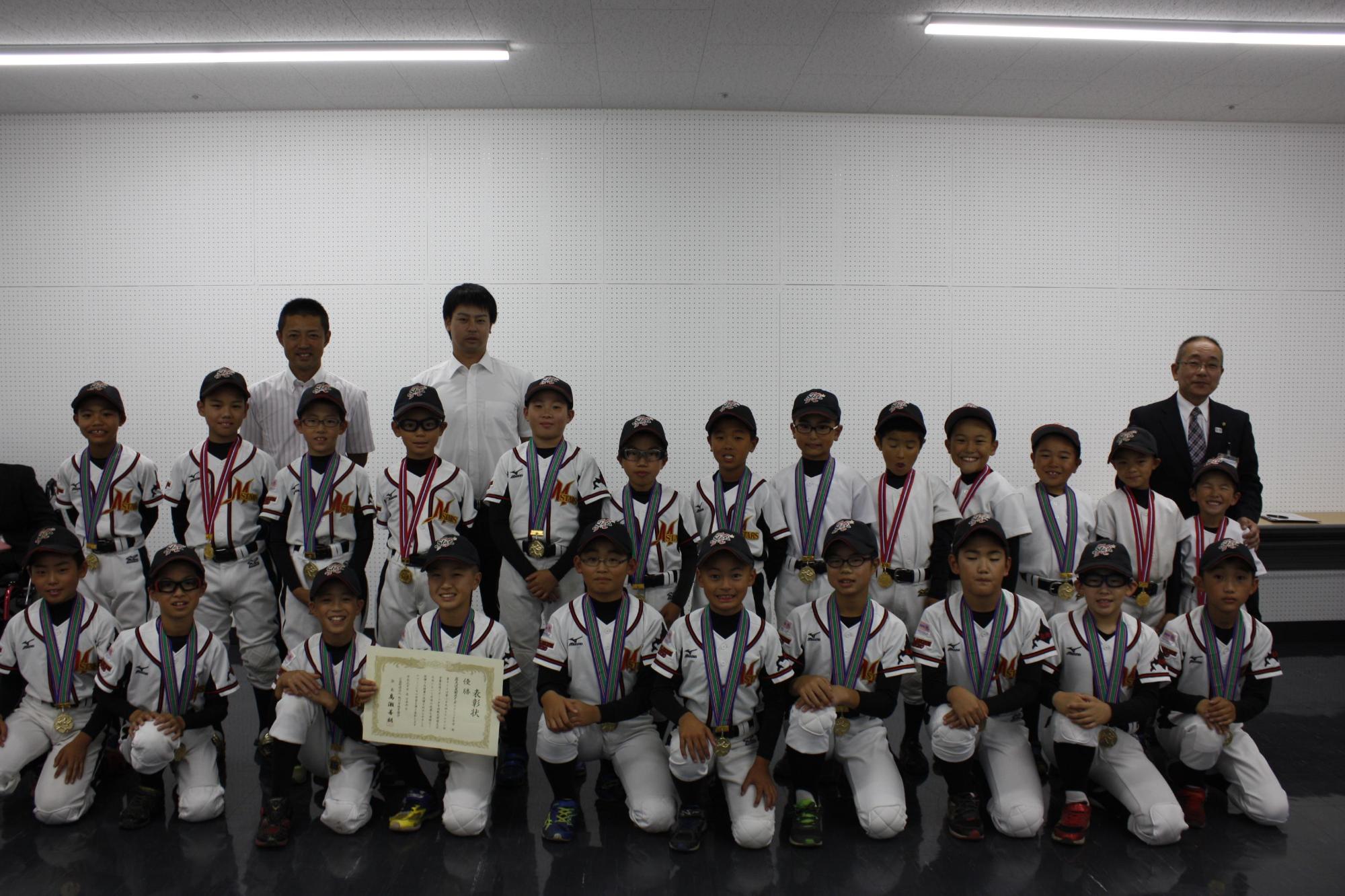 大会で優勝した記念の賞状を持ちメダルを首にかけて記念写真を撮っている少年野球団の皆さんの写真