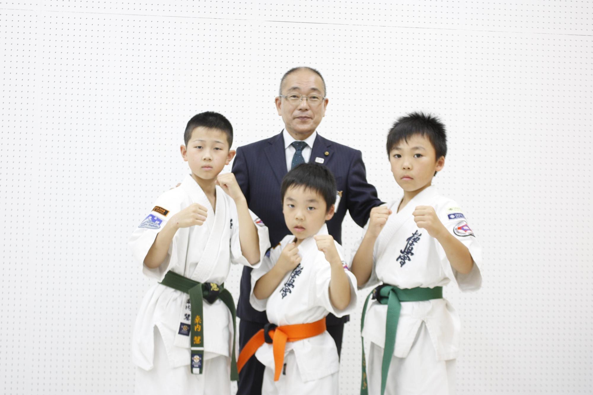 空手道着でポーズをとる3人の小学生と教育長の写真
