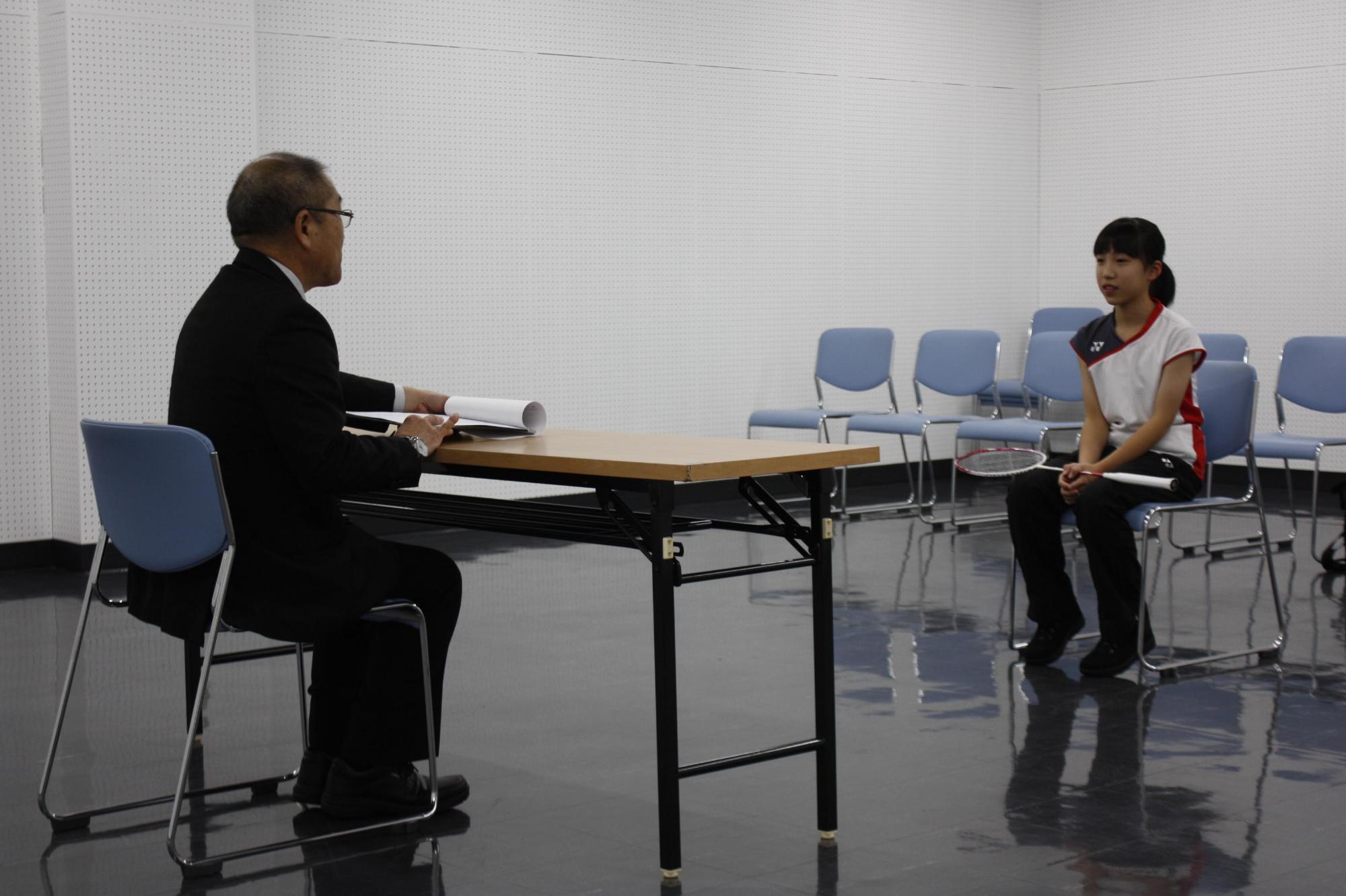 教育長とバトミントン学生選手が机を挟んで対面して座っている写真