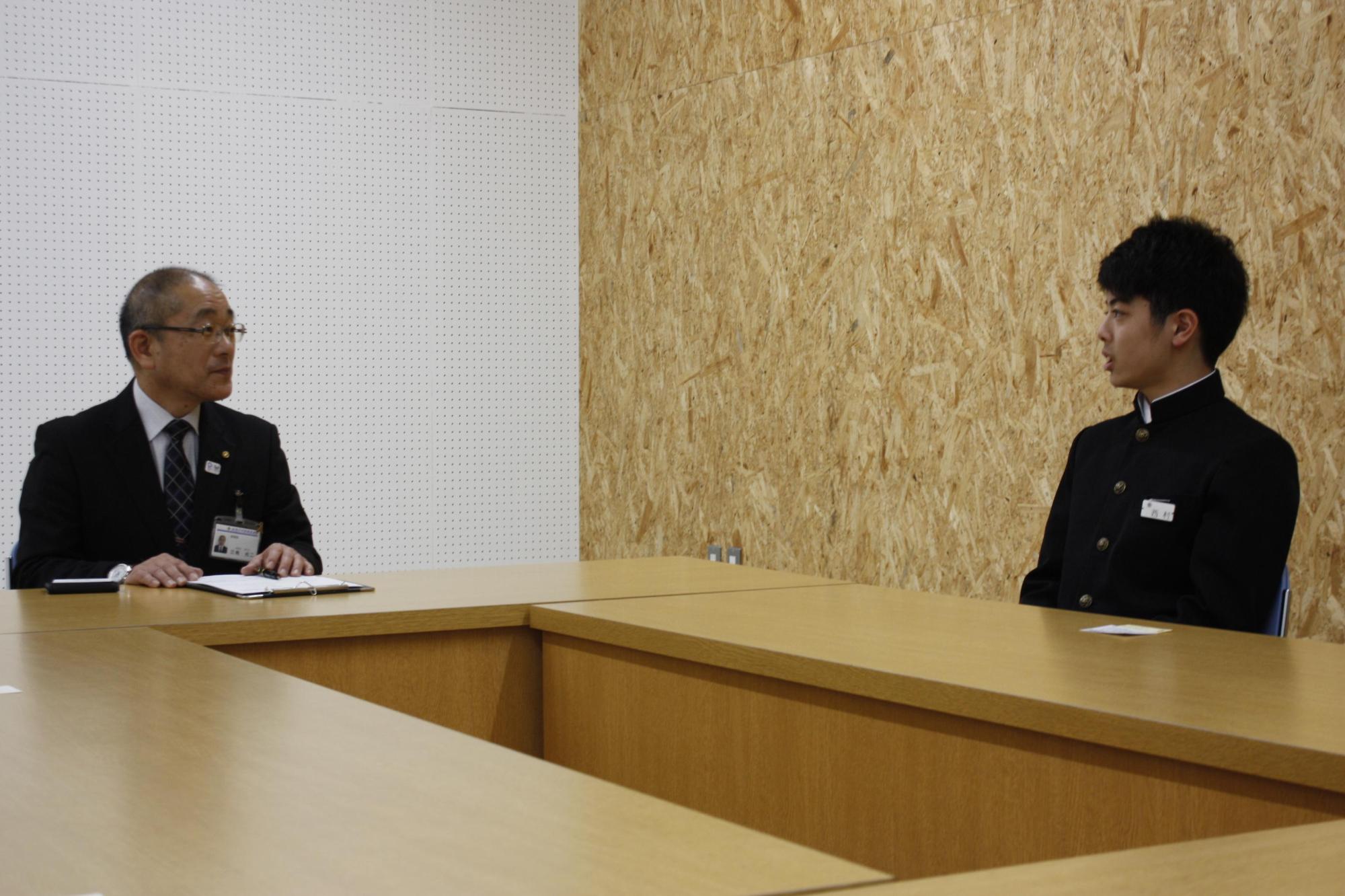 教育長と新体操選手の学生が机を囲んで斜めに対面している写真