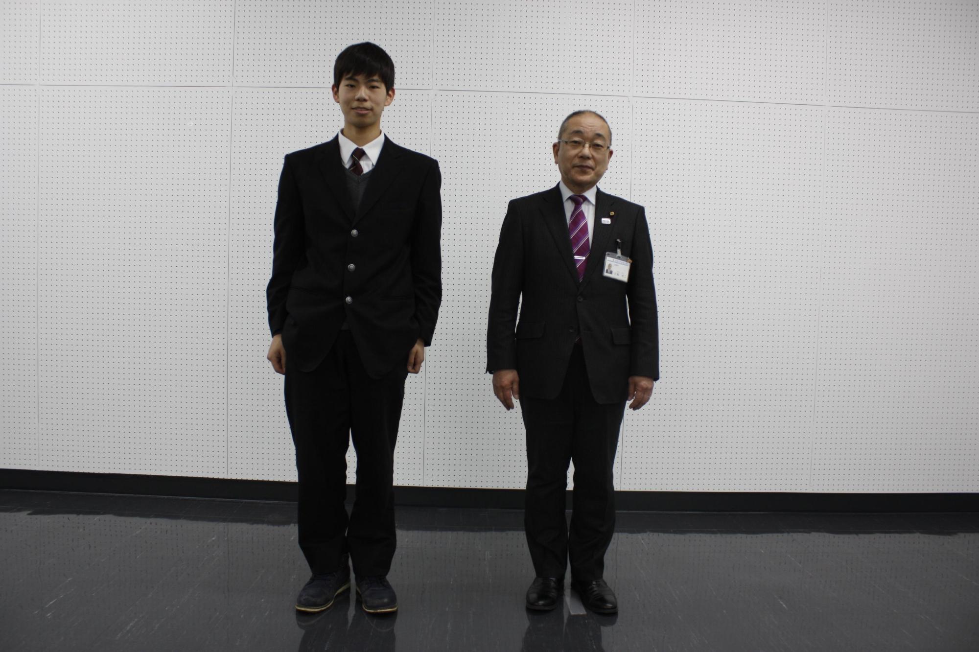 教育長の横で学生服を着た男子学生が笑顔の写真