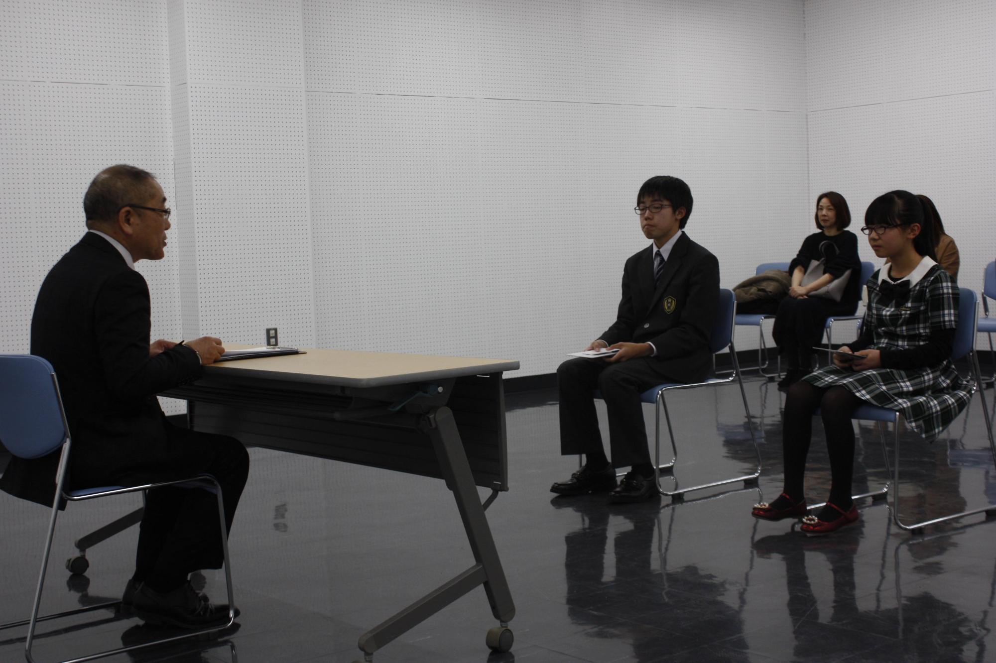 教育長の前に座っている男女二名の学生の写真