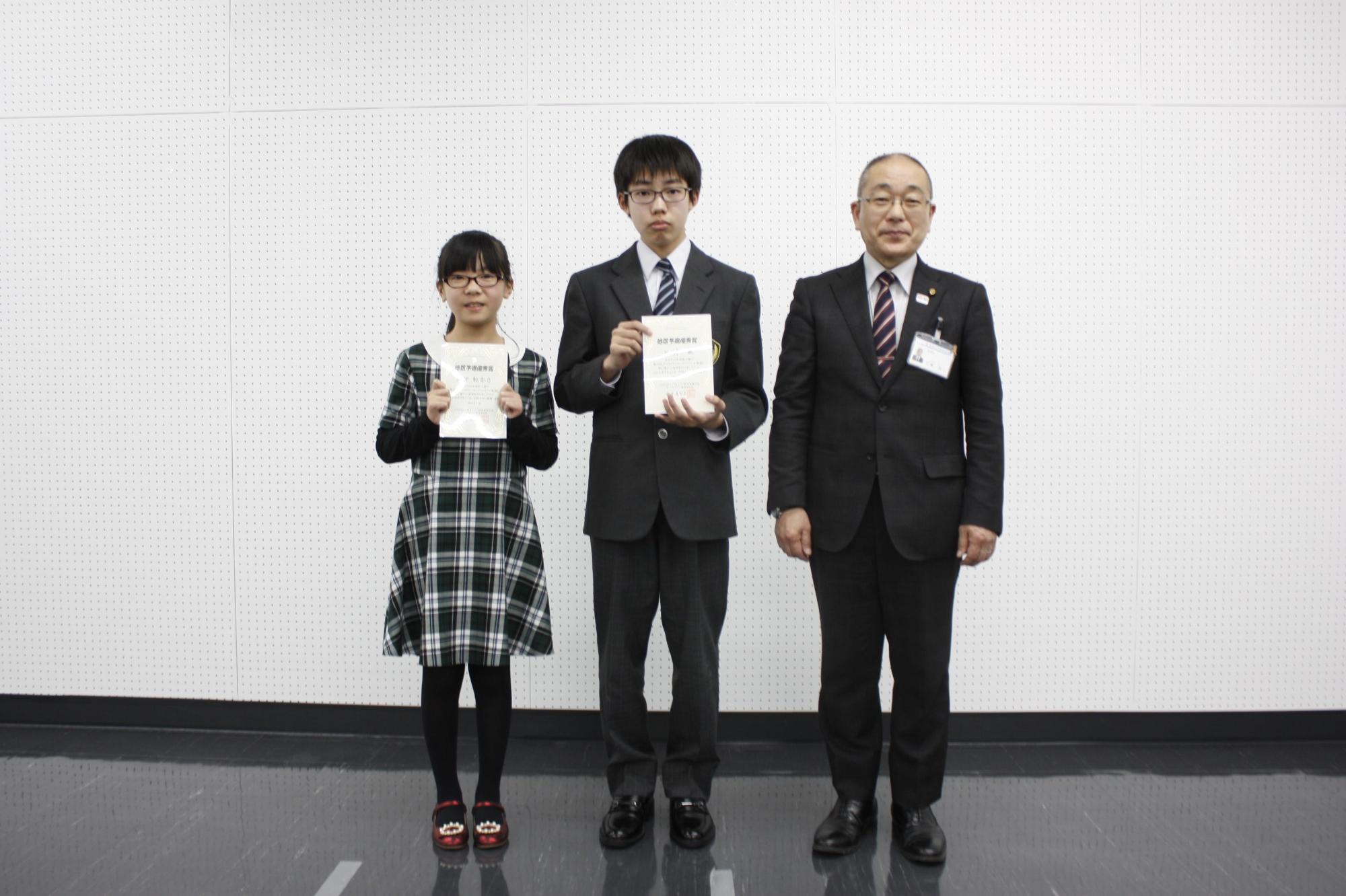 教育長の横で賞状を持っている男女の学生の写真