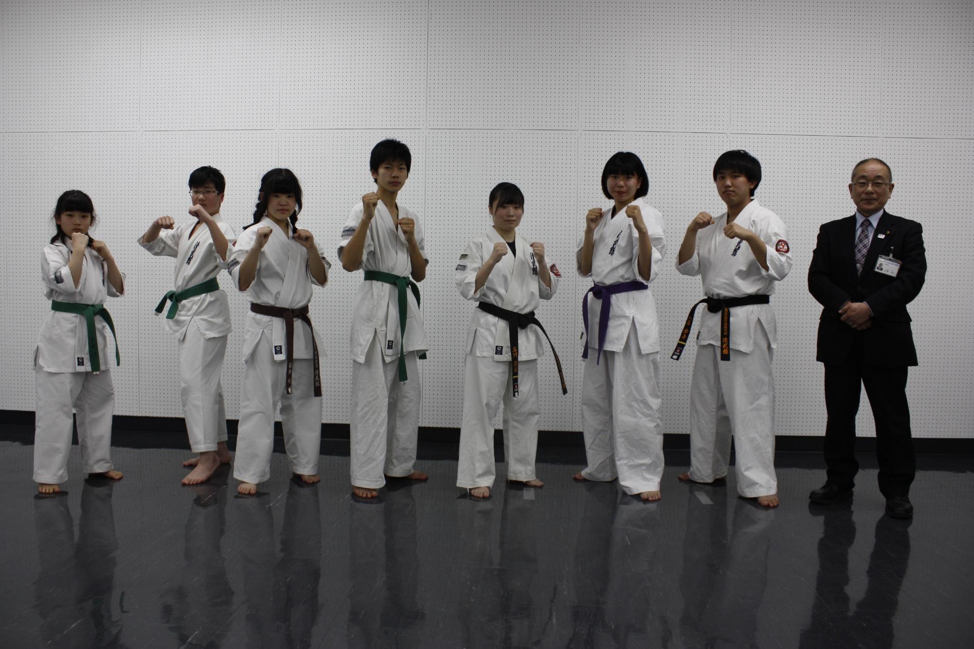 教育長の横で道着を着た学生たちが構えを見せていている写真