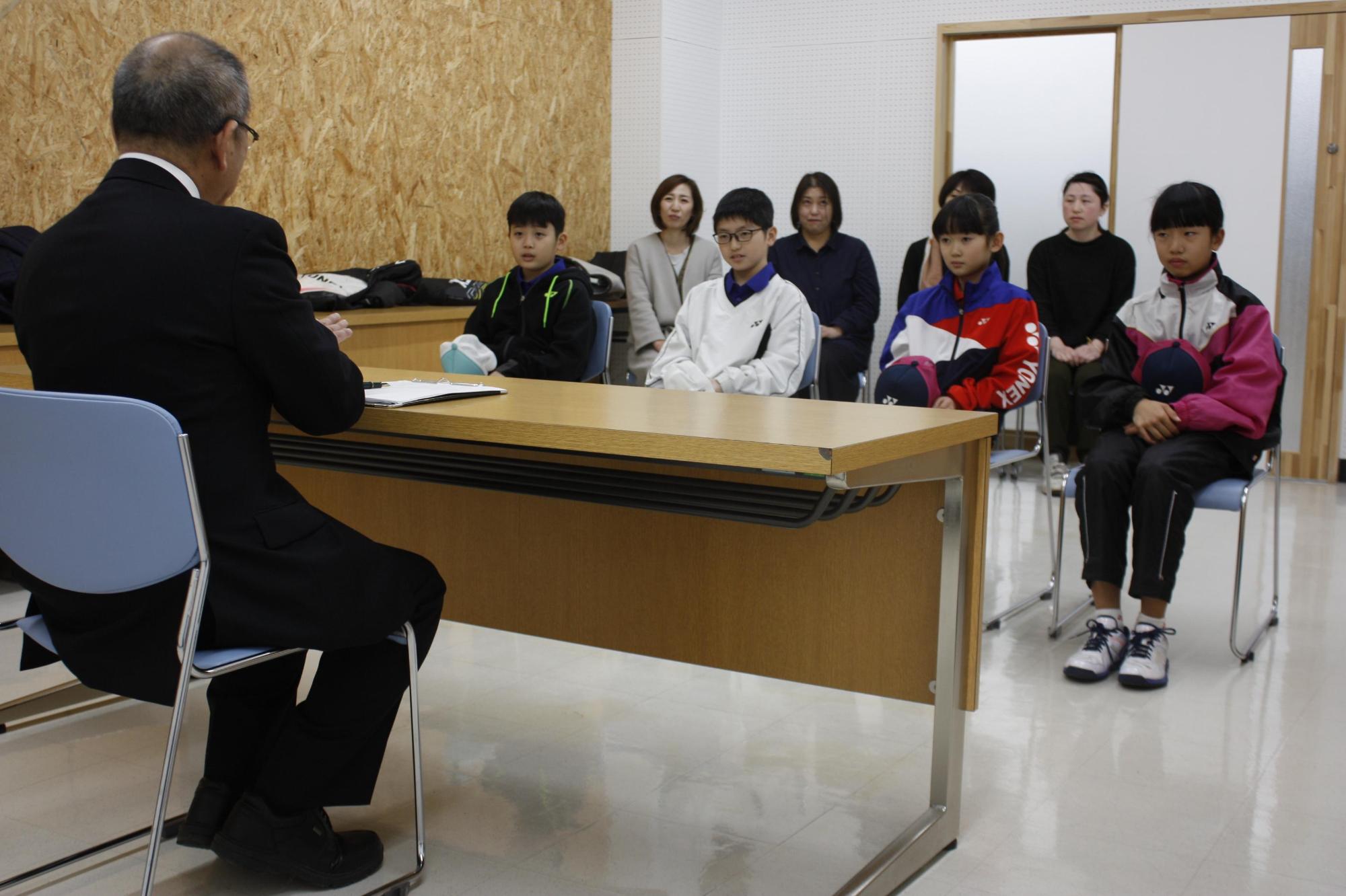 教育長の前に座っているテニスのユニフォームを着た児童たちの写真