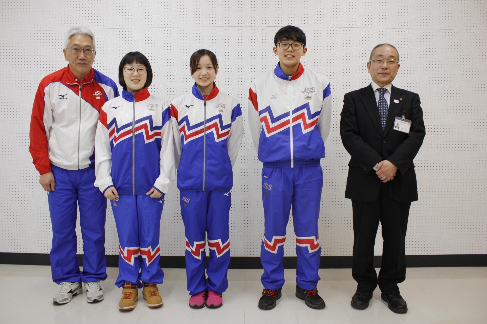 教育長の横で青と白のジャージを着た学生たちが笑顔の写真