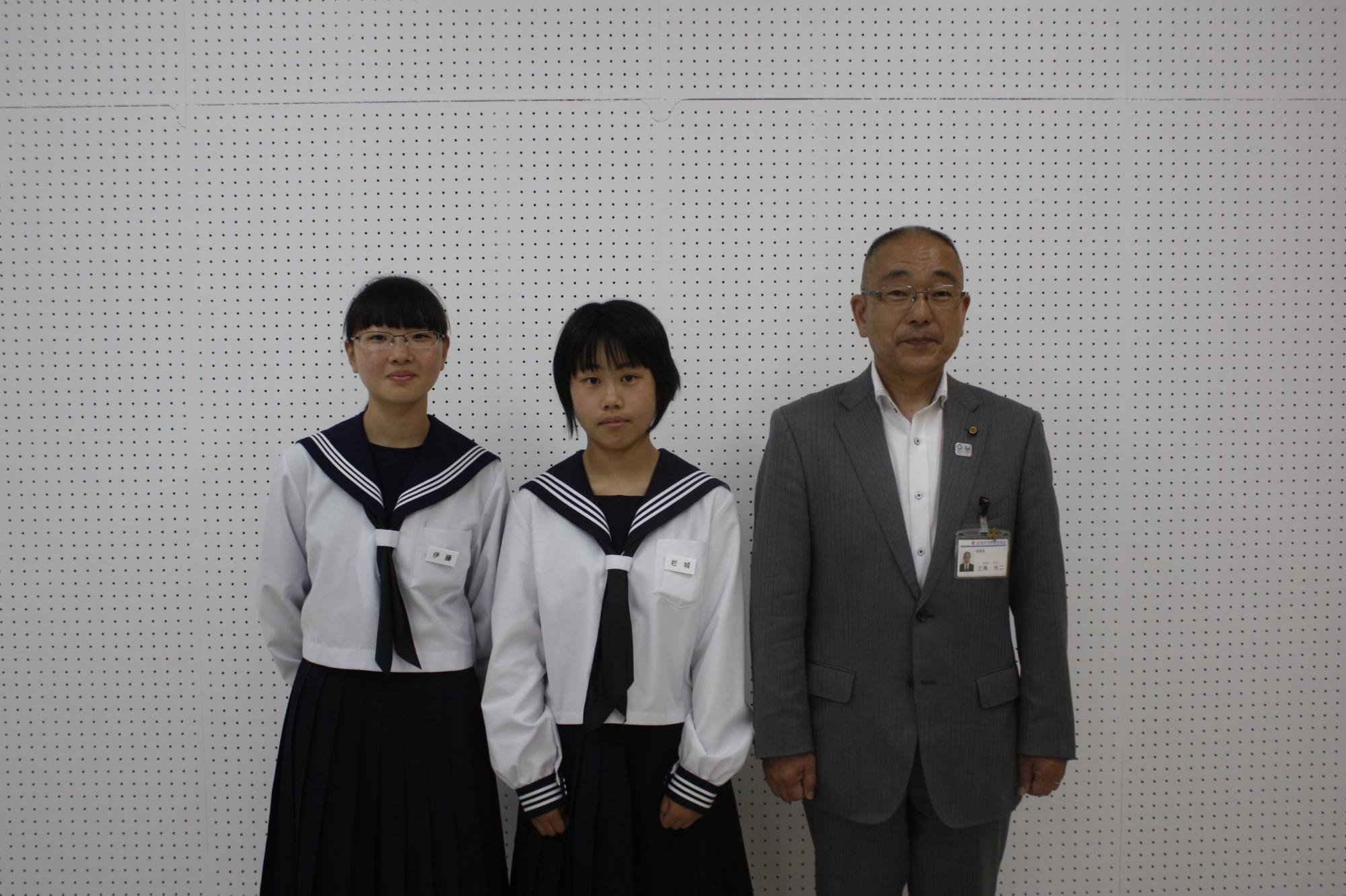 右からスーツを着た男性と2人の女子生徒が並んでいる写真