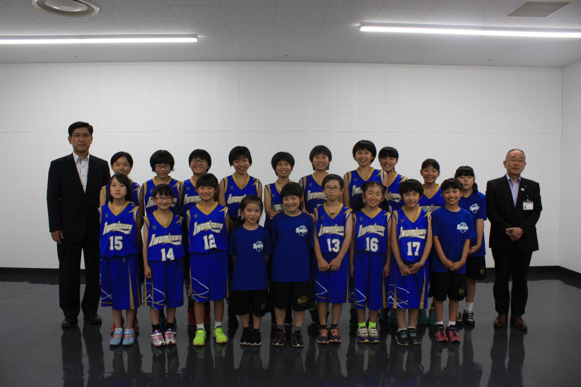 多くの子供たちが横に並び、その左右にスーツを着た男性が1人ずつだっている写真