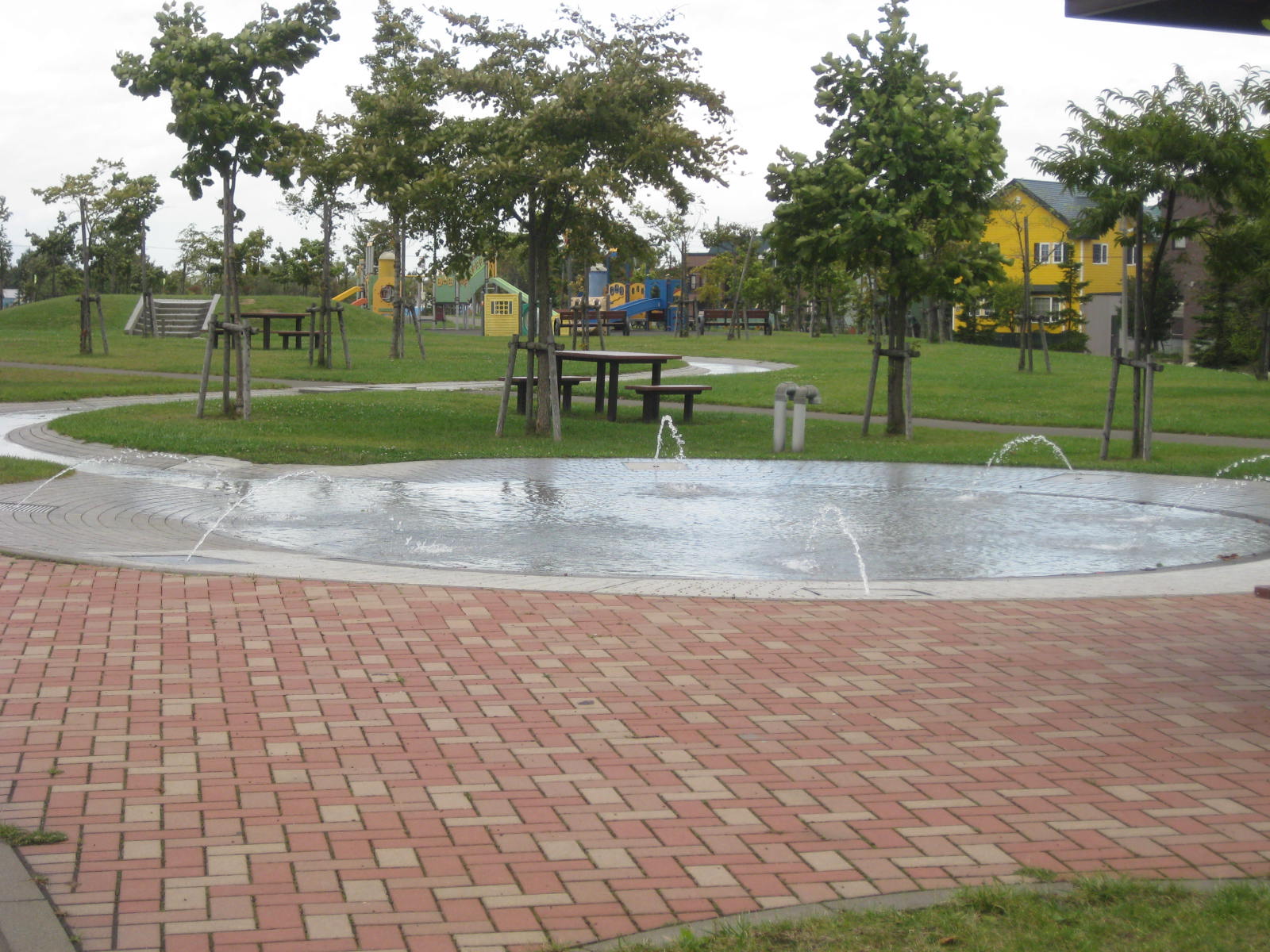 涼しげな噴水広場とベンチ、遊具が並んだ室蘭本線跡地緑地の写真