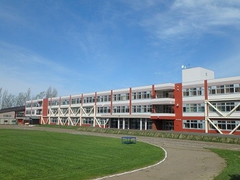 手前にグラウンド、奥に白に茶色がアクセントになっている校舎をグランド側から全体を写した南小学校の写真
