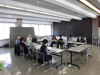 四角形に並べられた机の前の椅子に座りながら会議に参加する10名の人々を斜め前から撮った写真
