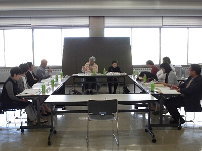 四角形に並べられた机の前の椅子に座りながら会議に参加する10名の人々を正面から撮った写真