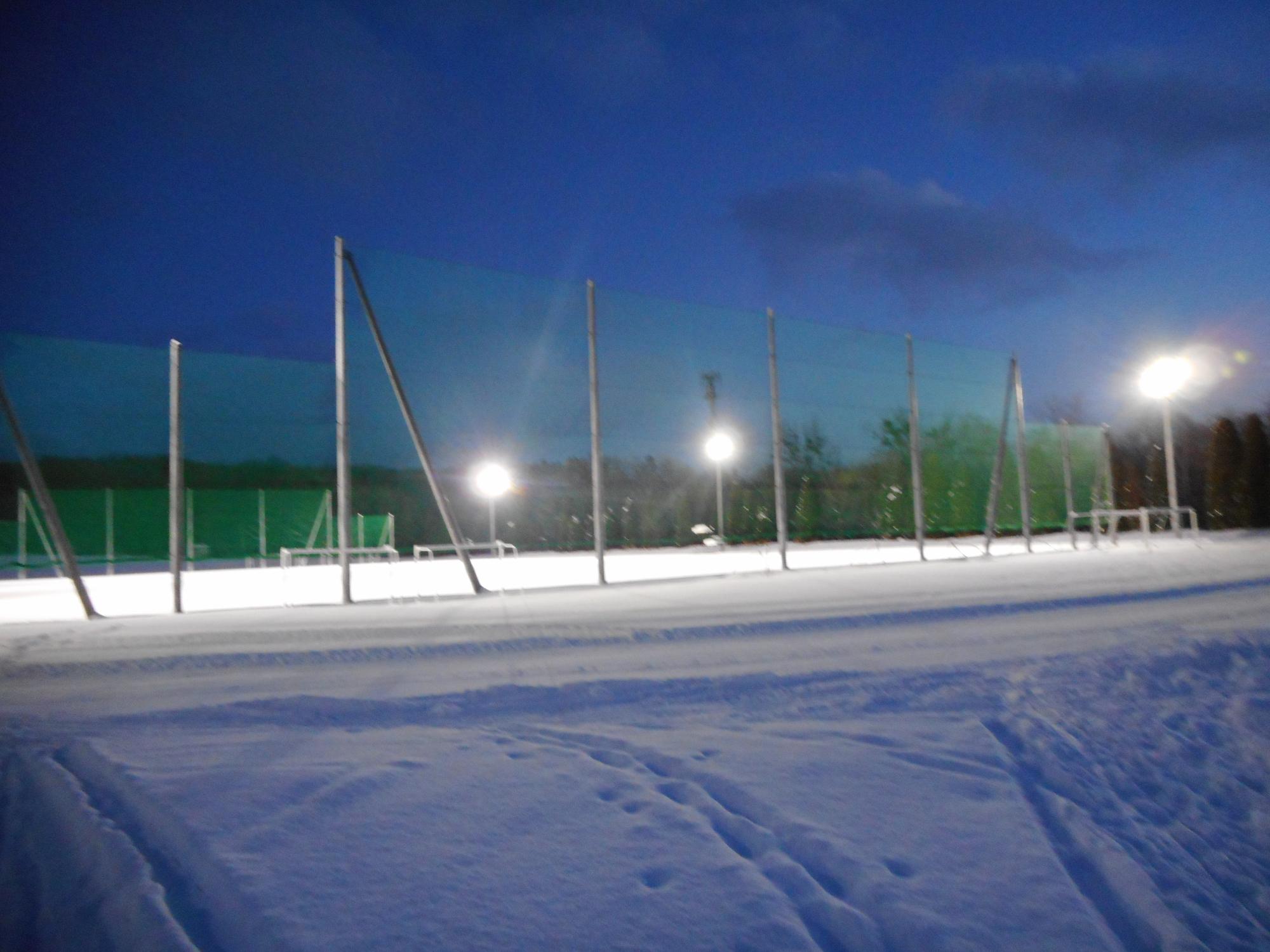 夜空の下、辺り一面雪に覆われたグラウンドに光る照明設備の写真