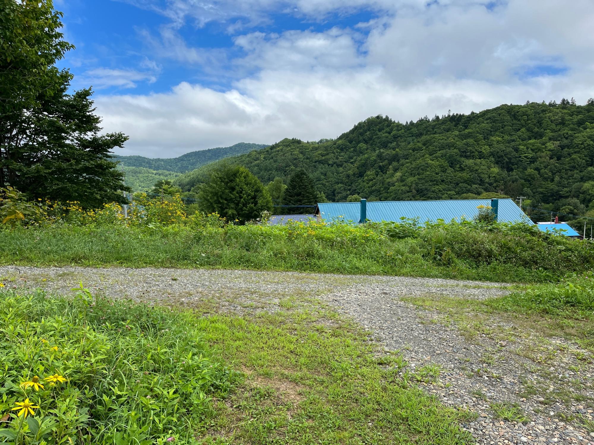 手前に未舗装の道路があり、奥に緑の山々と青空が広がるNORD houseからの風景