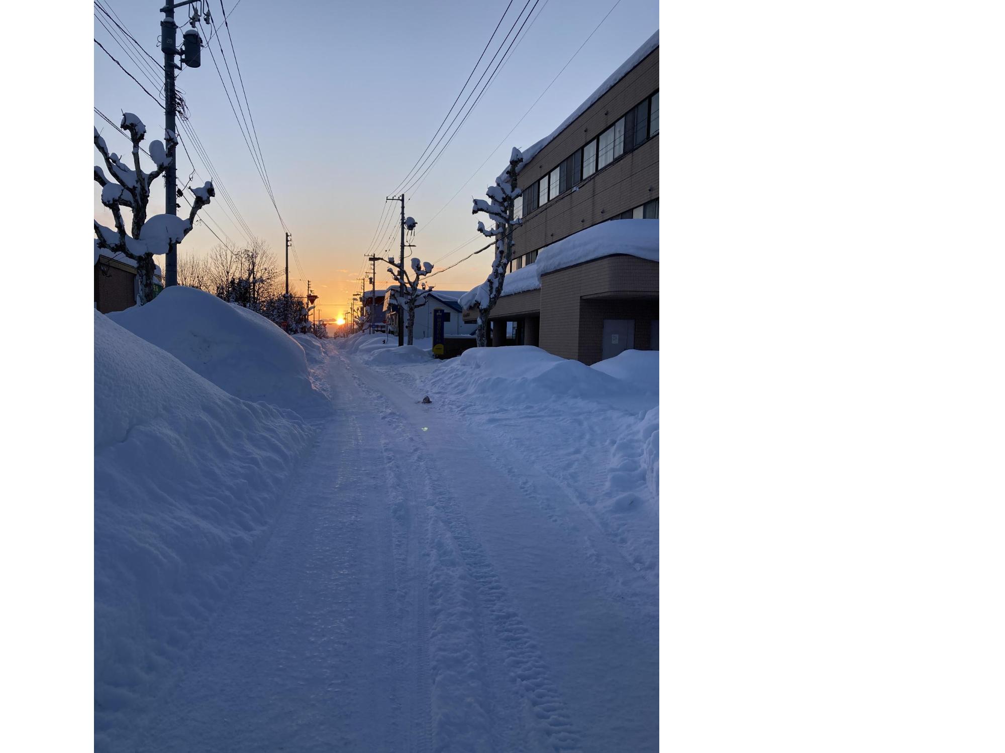 道路脇に積もった雪に沈んでいく夕日の写真