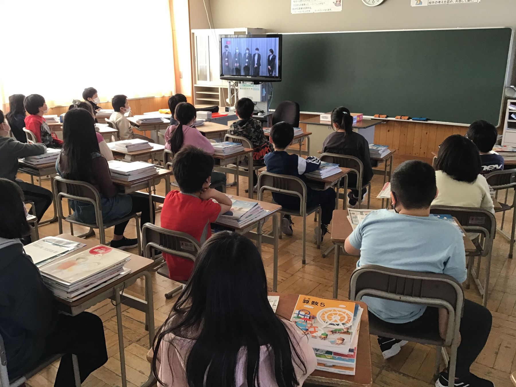 教室内で、教壇横に設置されたテレビを見ている児童達の写真
