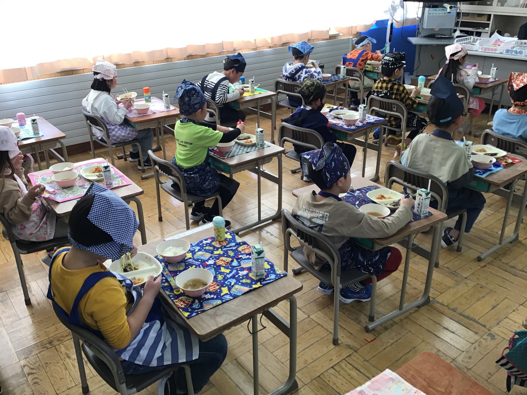 教室内で机に向かい、給食を食べているエプロン姿の児童達の写真