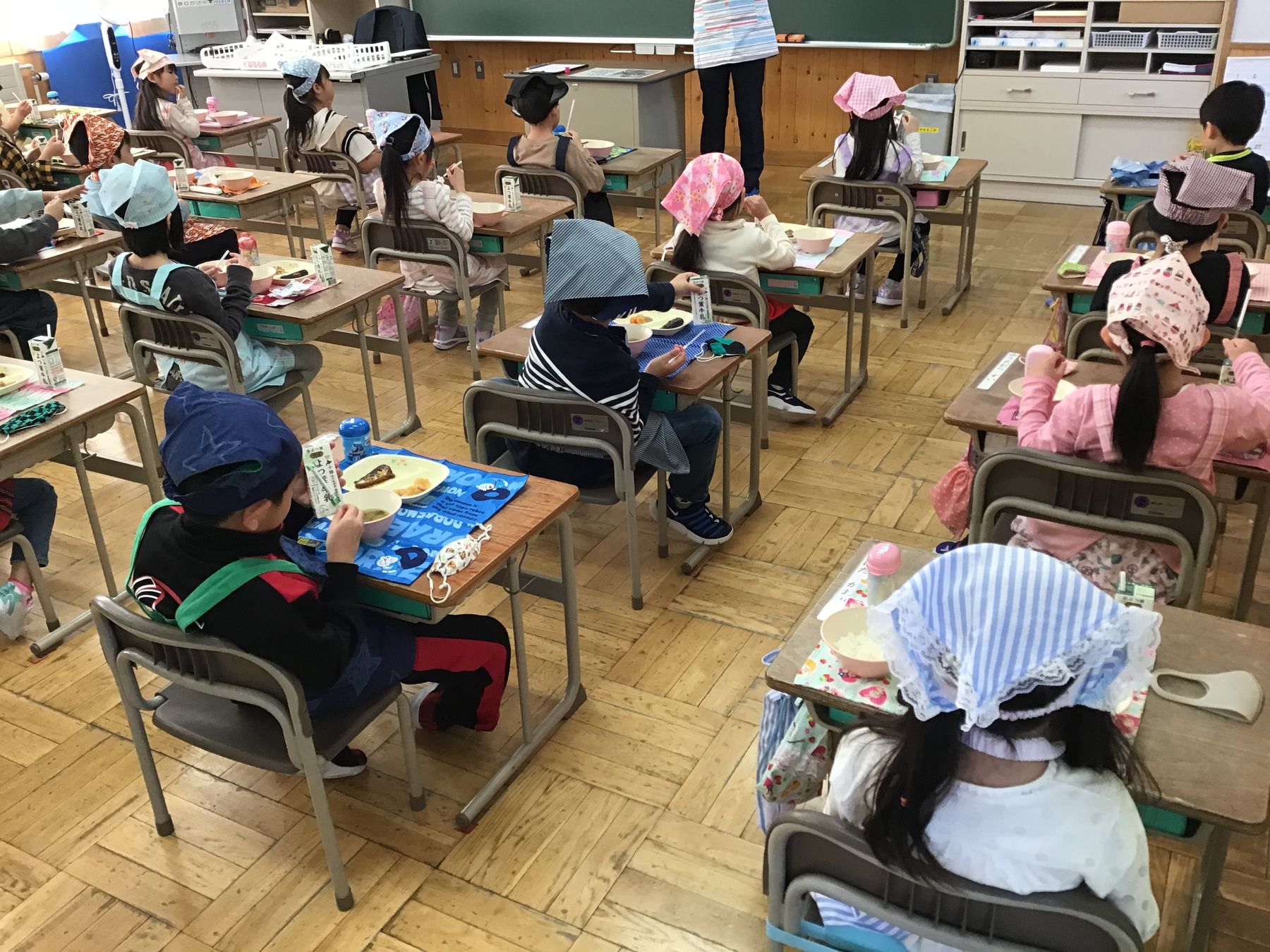 教室内で、エプロン姿の児童達が給食を食べている写真