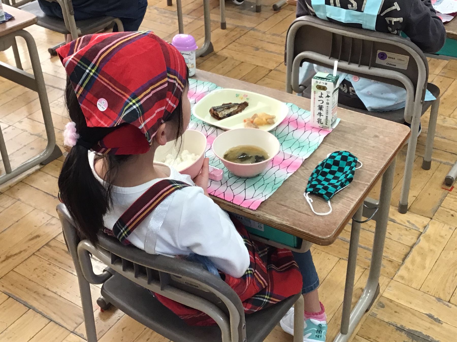 教室内で、給食を食べているエプロン姿の女の子の写真