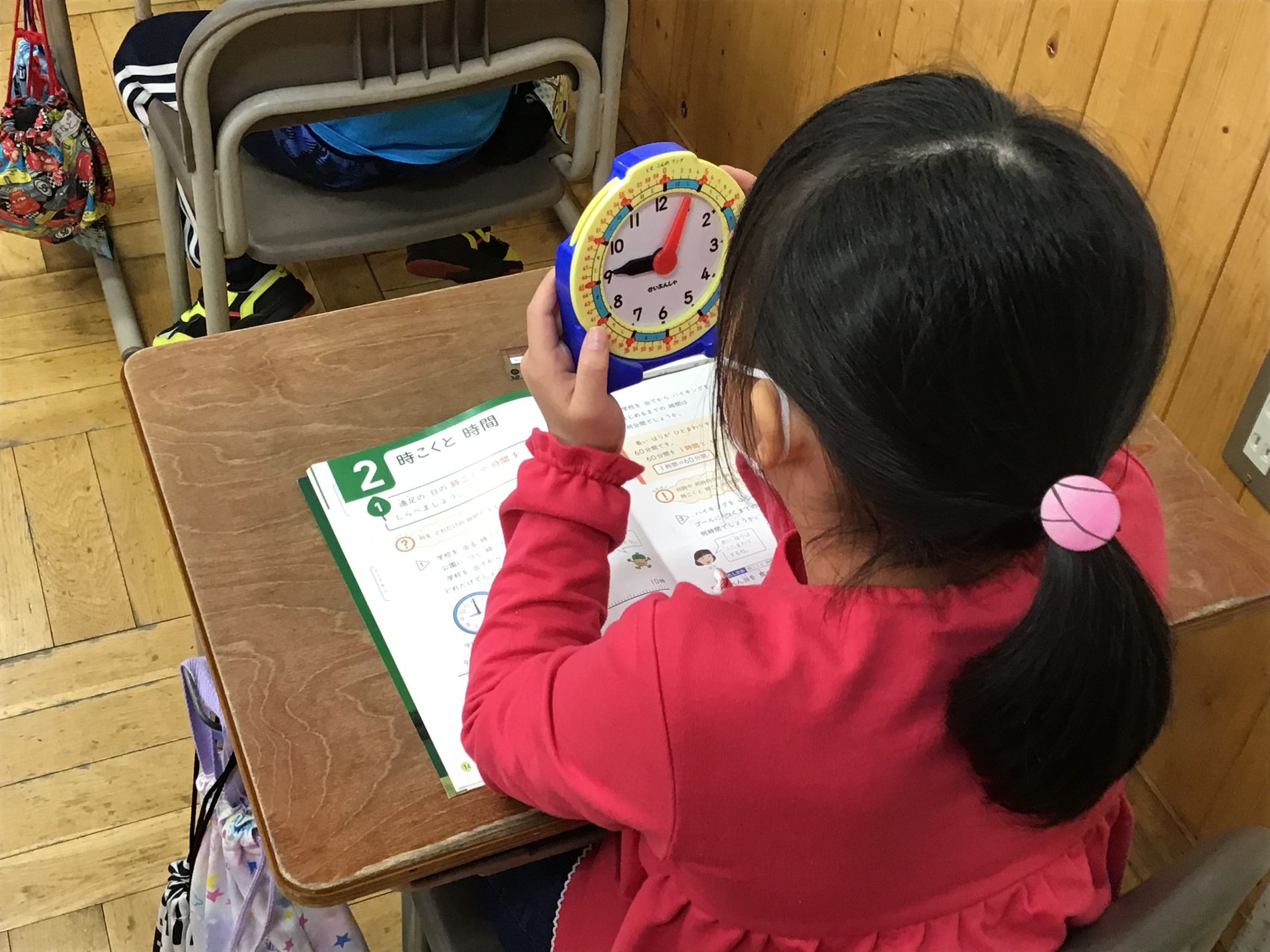 教室の机に向かった女子児童がプラスチック製の時計を見ている写真