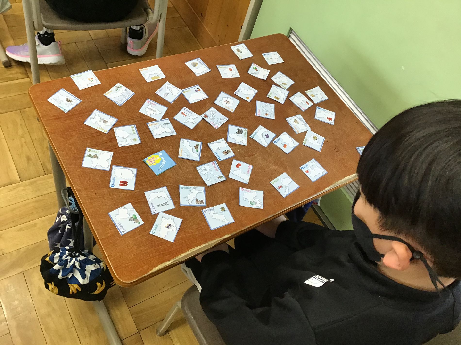 教室の机に向かった男子児童が机上に散らばった、各都道府県のカードを眺めている写真