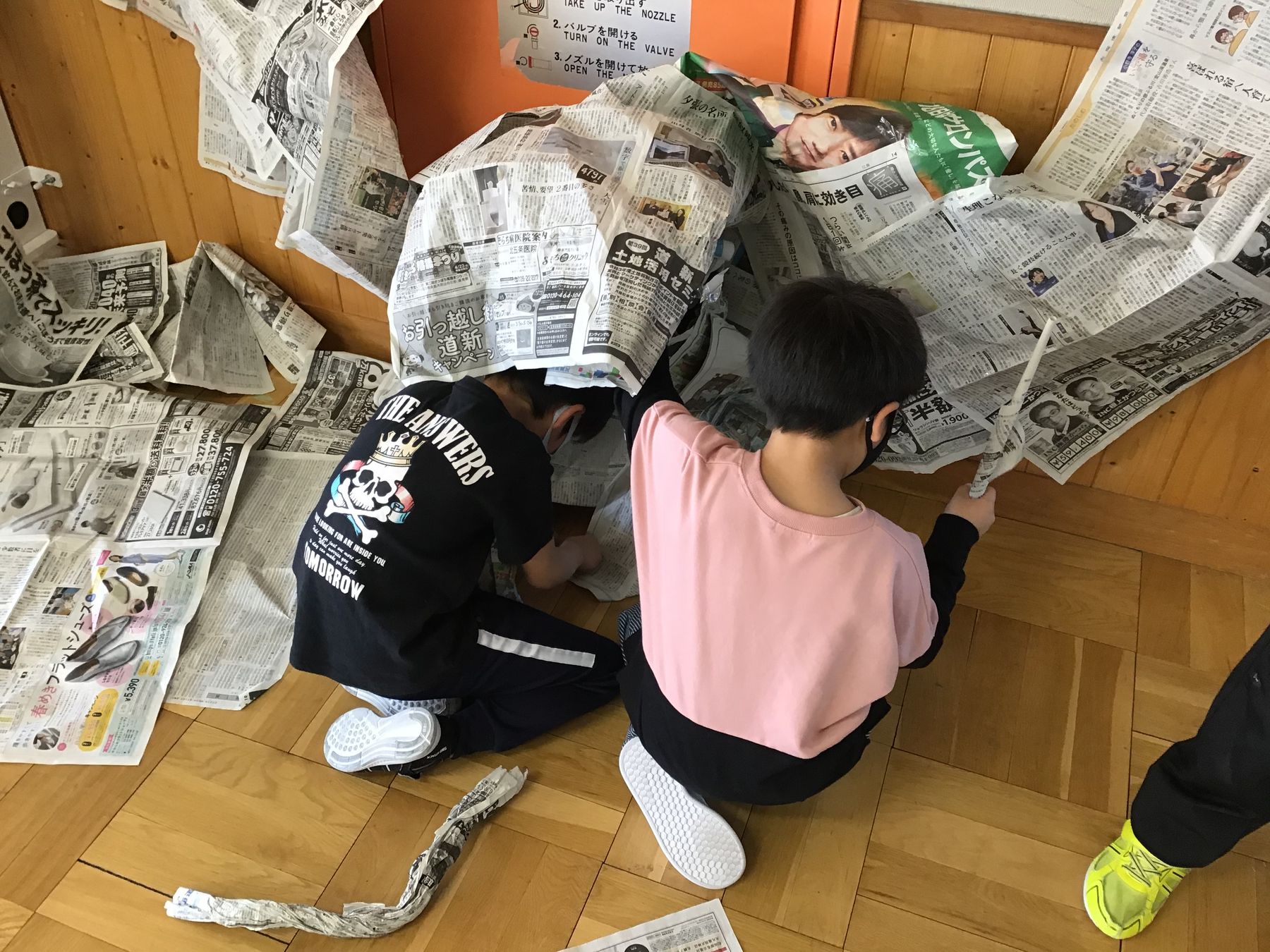 室内の床に座り新聞紙を切ったり丸めたりして工作をしている、2人の男の子の写真