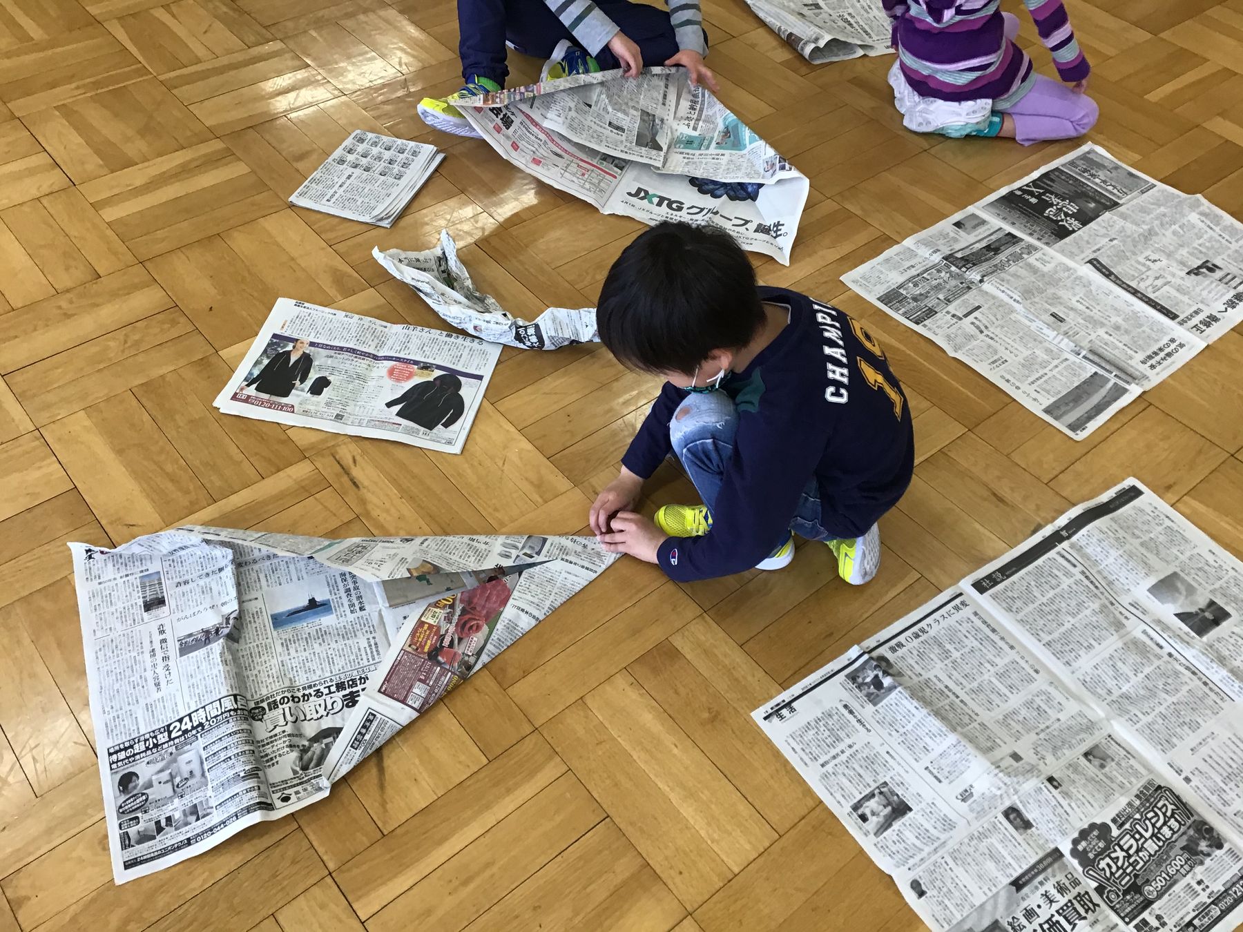 室内の床に座り新聞紙で紙飛行機を作ろうとしている、男の子の写真