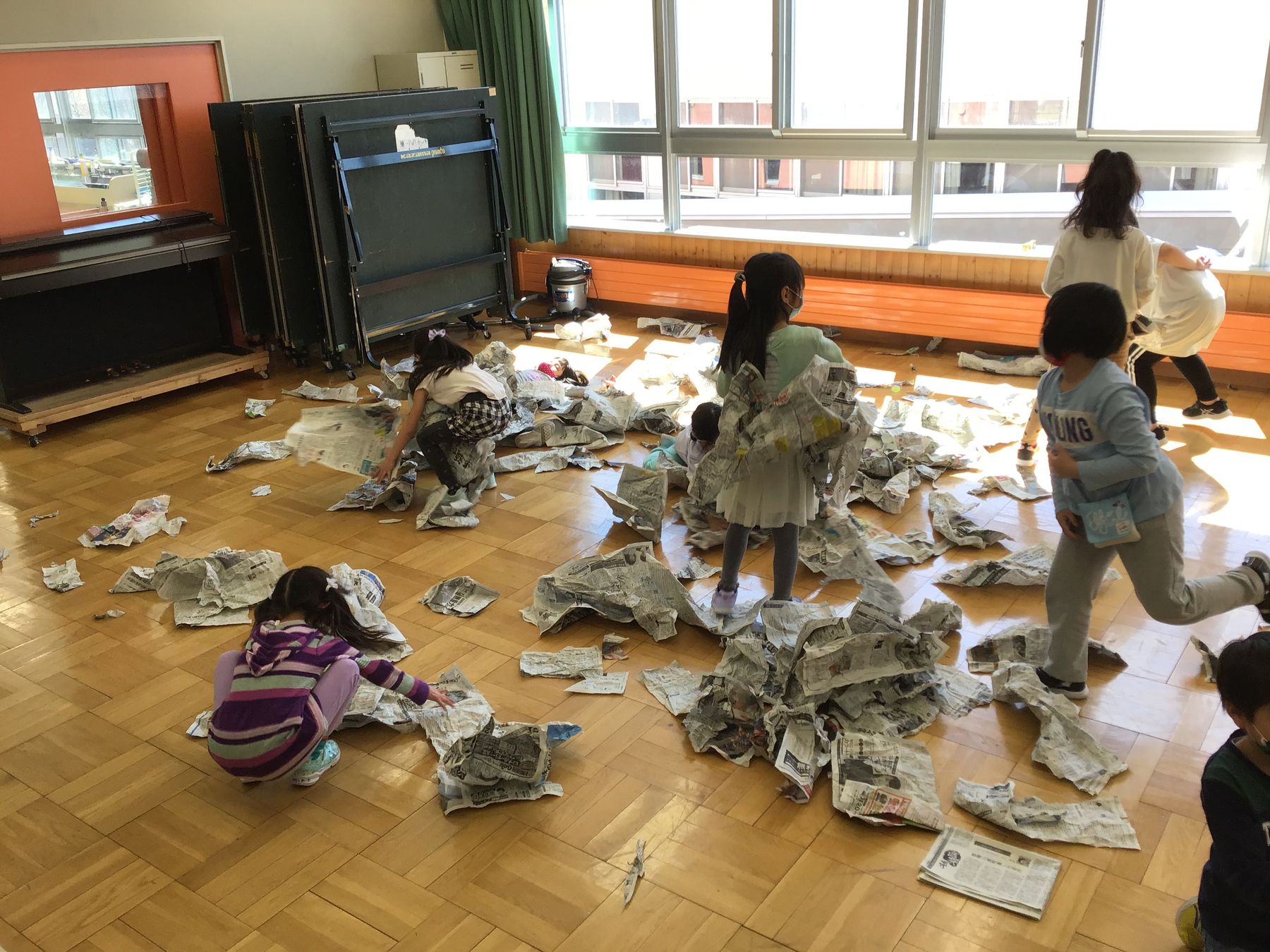 学校のホールで床に散らばった新聞紙を集める子供たちの写真