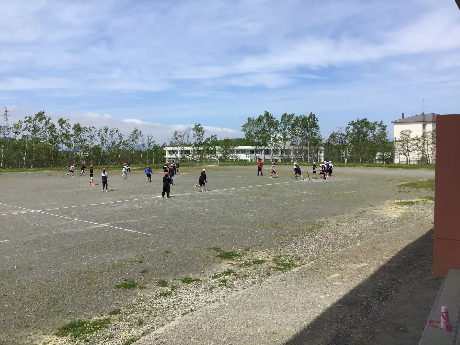 青空の下、学校のグラウンドで球を使って運動をしている、赤や白の帽子をかぶった子供たちの写真