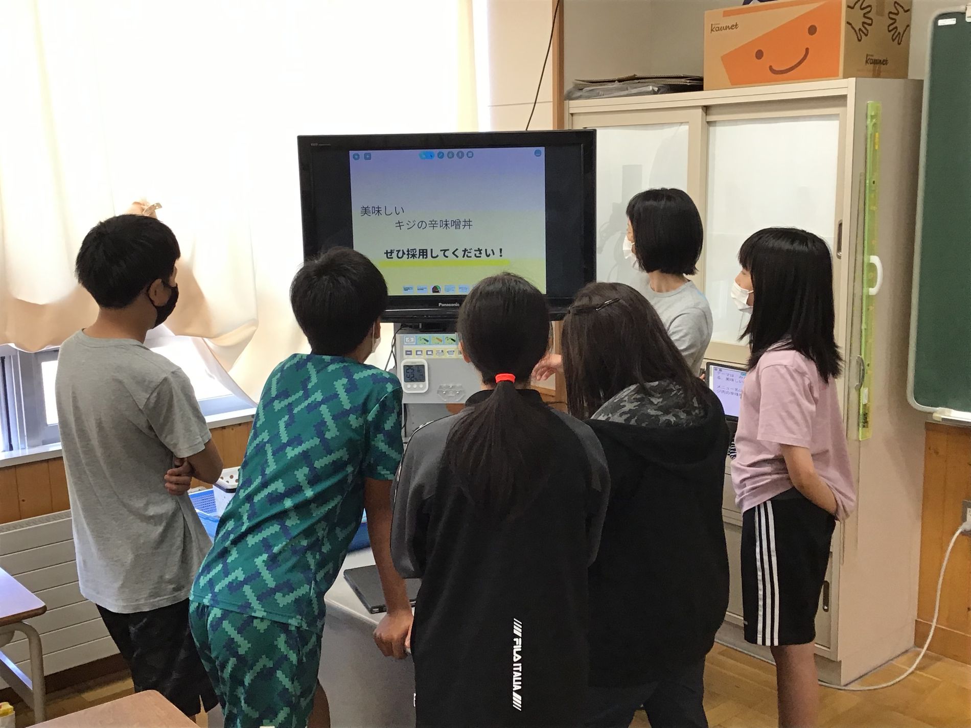 教室のモニターに映るメッセージを近くで見ている子供たちの写真