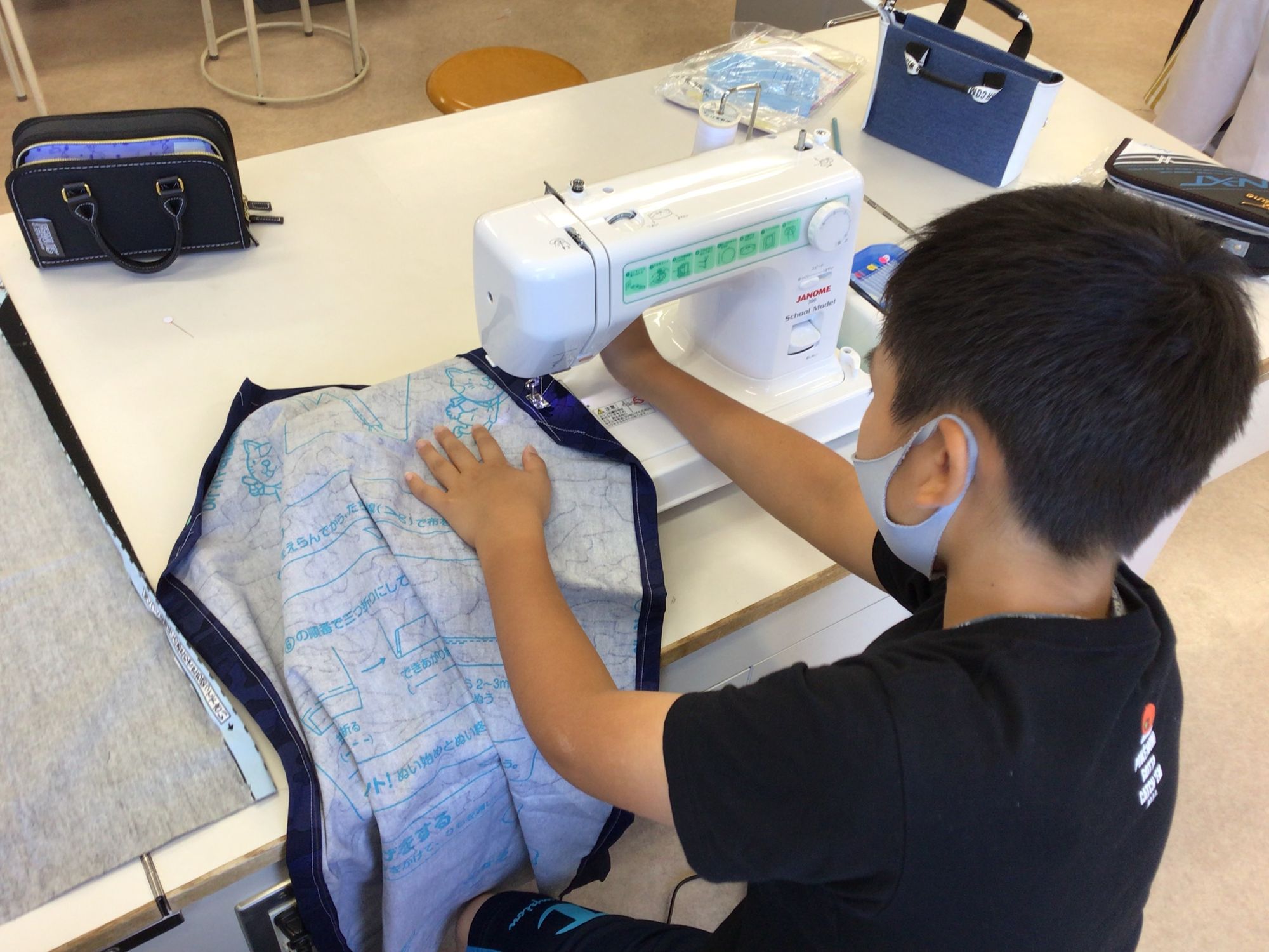 机の上のミシンを使い、紺色の生地を慎重に縫っている男の子の写真