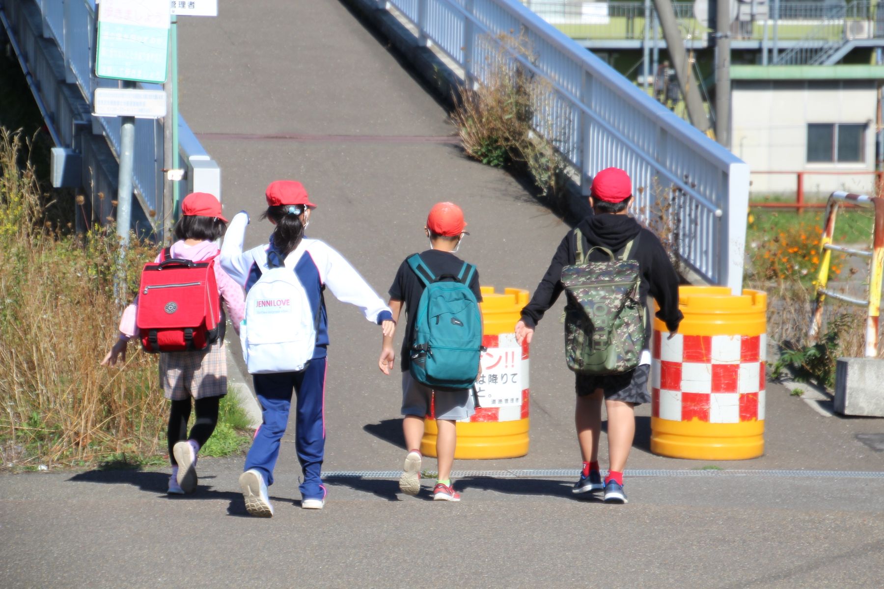 これから橋を渡ろうとする、赤い帽子をかぶりリュックを背負った4人の子供の写真