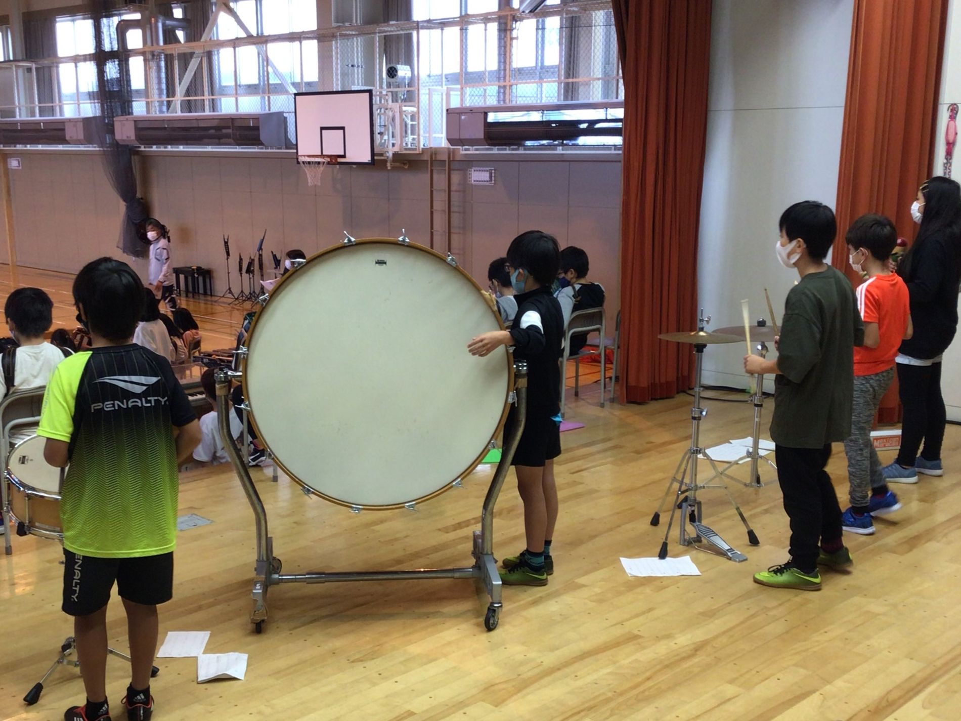体育館の舞台に立ち、大太鼓やシンバルを練習している子供たちの写真