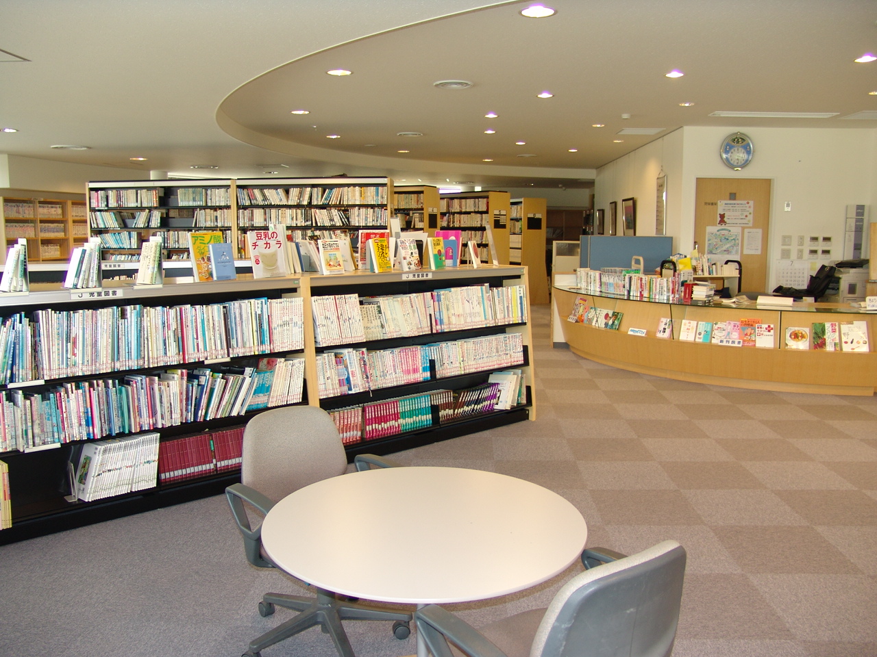 岩見沢市北村学習交流館にある1組のテーブルと椅子が配置されたスペースの奥にある本棚と貸し出しカウンターの写真