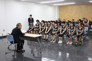 教育長表敬訪問にて岩見沢ミニバスケットボール少年団女子のみなさんが椅子に座りお話を聞いている姿の写真